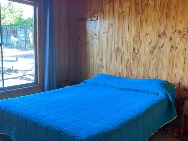 Dormitorio de cabaña con cama matrimonial y paredes de madera en Camping Porvenir