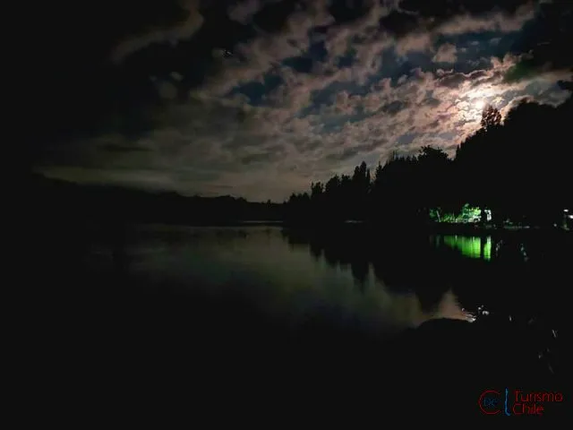 Vista nocturna del río Laja con luna llena y luces del camping reflejadas en el agua